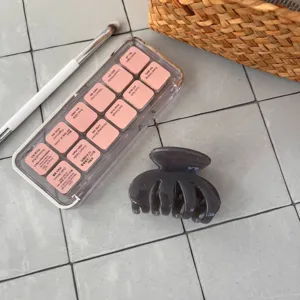 Nahaufnahme einer grauen Haarklammer auf gefliester Oberflaeche mit Make-up-Requisiten.