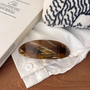 Detailed view of large oval hair clip with stylish tortoise shell pattern and golden lettering.