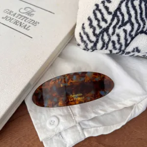 Detailed view of the large tortoise shell pattern spring hair clip featuring gold letter print.