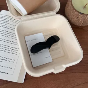 Vista detallada de una elegante pinza de pelo negra en forma de corazón en una caja ecológica.