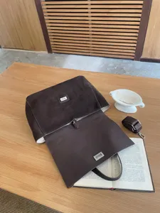 Brown suede tote bag with flap closure and metallic lock, featuring adjustable shoulder strap.