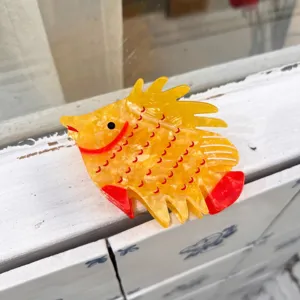 Dettaglio molletta per capelli in acetato a forma di pesce, colore vivace, presa salda e carina.