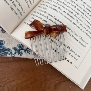 Close-up of a tortoiseshell acetate bow hair comb placed on an open book, detail view.