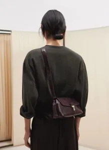 Detailed rear view showcasing a retro dark brown leather messenger bag worn crossbody style.