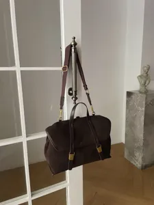 Dark brown suede messenger bag detail hanging on a vintage door handle with metal hardware