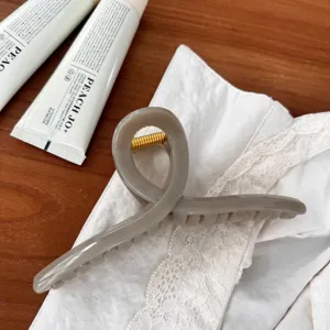 Detailansicht einer stilvollen grauen geometrischen Haarklammer mit Goldfeder für Frisuren.