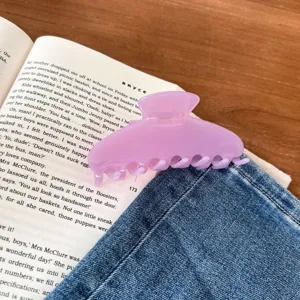 Paarse doorzichtige haarklem detailopname, elegante acetaat haarklem op een boek en spijkerbroek.