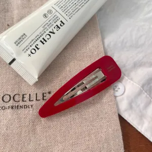 Gros plan détaillé d'une pince à cheveux rouge en forme de goutte sur une pochette en toile.