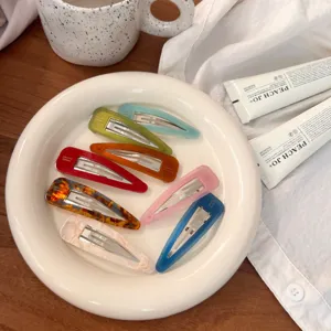 Détail de set de pinces à cheveux goutte colorées, mise en scène esthétique sur plat en céramique.