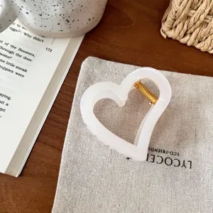 Detailansicht einer süßen weißen Herz Haarklammer mit goldener Feder, elegantes Haaraccessoire.
