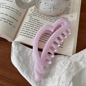 Primer plano detallado de una bonita pinza de pelo rosa en forma de corazón sobre libro.