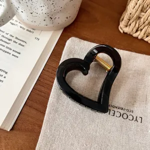 Detailaufnahme einer schwarzen herzförmigen Haarklammer mit goldener Feder. Schick.