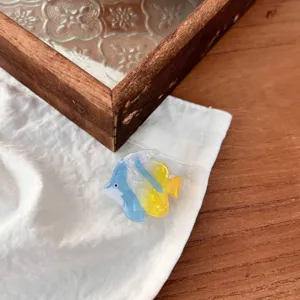 Detalle en primer plano de la pinza de pelo de pez pequeño de resina en azul y amarillo, estilo fresco.