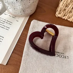Nahaufnahme einer dunkelroten herzförmigen Haarklammer mit goldener Feder auf Leinen.