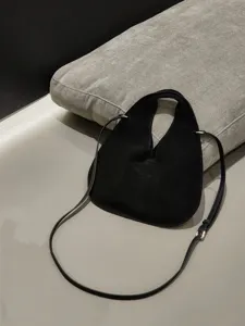 Detailed close-up view of the black suede triangular crossbody handbag on grey cushion.
