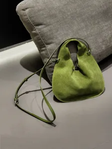 Green suede triangular dumpling bag close-up, showing soft leather texture and slim strap.