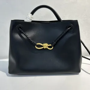 Black leather handbag with elegant woven straps and gold knot hardware for women.