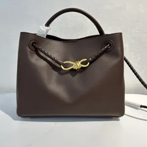 Dark brown leather handbag detail with elegant gold bow hardware and braided leather strap accent.