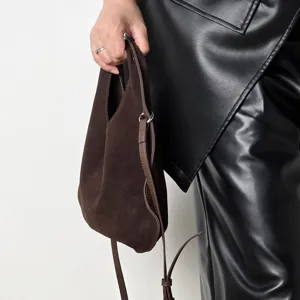 Close-up view of a dark brown suede triangular dumpling handbag showing fine texture and strap.
