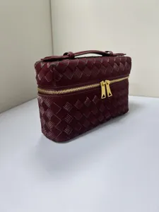 Glossy woven vanity bag detail, elegant burgundy cosmetic handbag with gold zipper hardware.