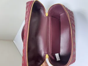 Detailed view of luxury woven leather cosmetic bag in rich burgundy with gold zipper and lining.