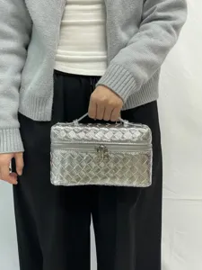 Silver woven vanity case detail view, featuring glossy intrecciato texture and zippers.