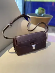 Close-up detail of dark brown leather messenger bag with metal lock clasp and texture.
