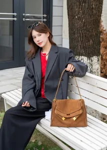 Detail view of brown suede shoulder tote bag with metal closure in outdoor setting.