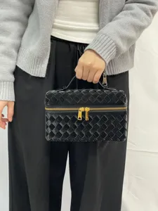 Detail shot of the black glossy woven cosmetic bag featuring gold hardware and sturdy handle.