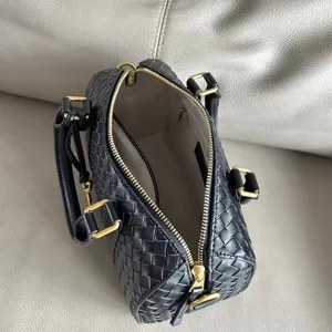 Close-up detail of black woven leather boston handbag with luxury gold hardware zipper.