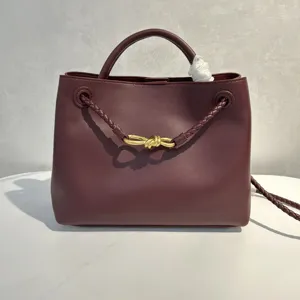 Burgundy smooth leather handbag with braided strap and elegant gold knot hardware detail.