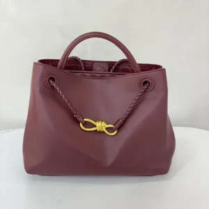 Burgundy leather handbag detail featuring braided strap and gold knot hardware closure.