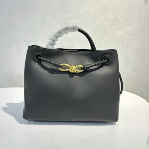 Black leather handbag detail showing the signature gold knot hardware and braided strap.