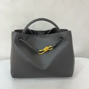 Dark grey smooth calfskin handbag featuring a stylish gold-tone metal knot and braided handles.