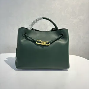 Dark green leather handbag detail featuring elegant golden bow metal hardware and braided handle.
