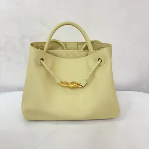 Butter yellow leather handbag with gold knot hardware and chic braided handle design.