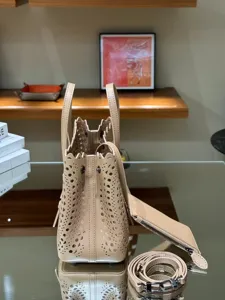 Beige leather laser-cut tote bag with top handles, detachable strap, and matching pouch.