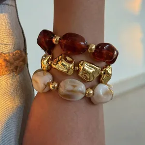 Nahaufnahme gestapelter geometrischer Perlenarmbänder mit unregelmäßigen Harz- und Goldkugeln.