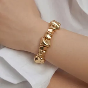 Detailaufnahme eines klobigen unregelmäßigen Goldarmbands am Handgelenk für den Alltag.