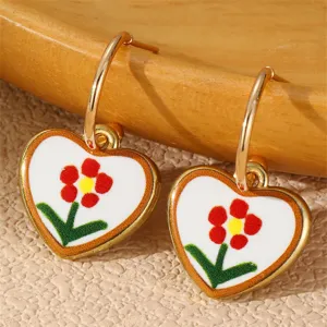 Nahaufnahme von goldgeränderten Herzohrringen mit süßem Blumen Emaille Design für den Alltag.