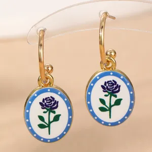 Nahaufnahme der eleganten goldenen Creolen mit ovalen Anhängern im blauen Rosendesign.