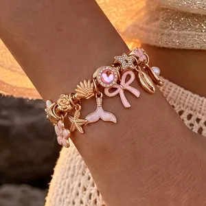 Goldfarbenes Charm Armband Detail mit niedlichen rosa Anhängern, Seestern und Kristallelementen.