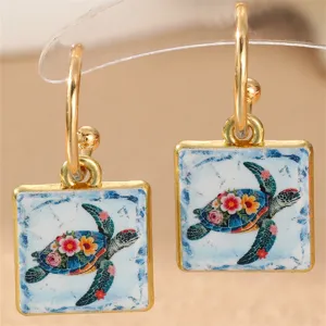 Nahaufnahme goldener quadratischer Keramikohrringe mit Meereskröten- und Blumenmustern.
