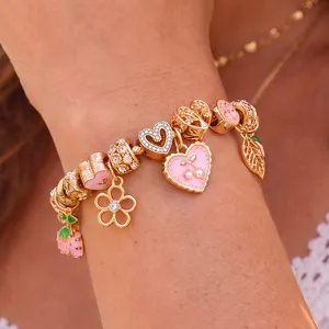 Goldfarbenes DIY-Charm-Armband Detail mit rosa Emaile-Herzen, Blumen- und Erdbeeranhängern.