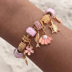 Detailaufnahme des goldfarbenen DIY-Bettelarmbands mit rosa Perlen und süßen Meeresanhängern.