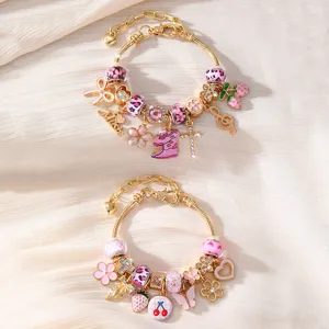 Detailaufnahme vergoldeter DIY Bettelarmbänder mit rosafarbenen Emaille-Anhängern und Perlen.