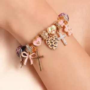 Detailansicht des modischen DIY Bettelarmbands mit rosa Schleife, Kreuz und Leo-Herz Anhängern.
