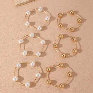 Set de 6 pulseras de cadena dorada apilables con perlas blancas y cuentas metálicas.