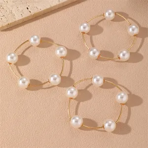Primer plano de delicadas pulseras de alambre dorado con elegantes perlas falsas.