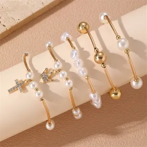 Set de pulseras en capas doradas con perlas, dijes de cruz y corona, joyería elegante.